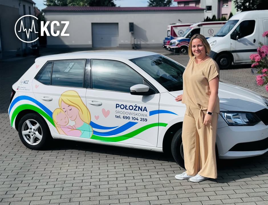 Polożna obok auta z logo.