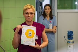 Kobieta z certyfikatem, druga osoba w tle.